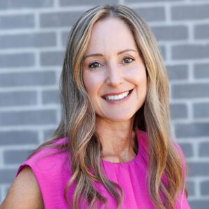 Lori wearing a bright pink top and smiling at the camera