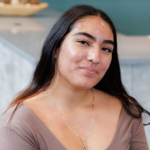 Lesly wearing a light brown top and smiling at the camera