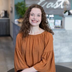 Lauren - female sitting posing wearing an orange shirt with brown curly hair