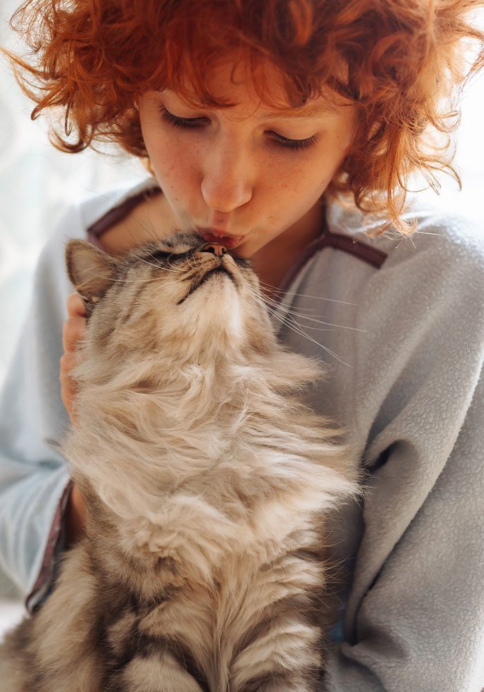 woman with short curly red hair kissing fluffy cat on nose